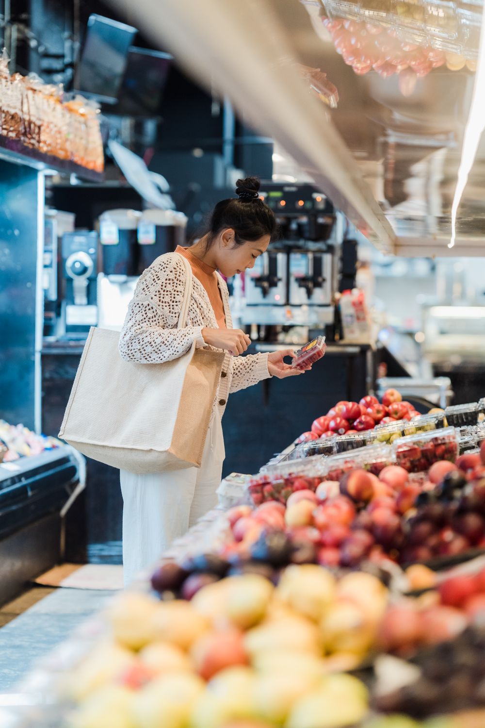 A shopper checking a packet of berries beside colourful fresh fruit.