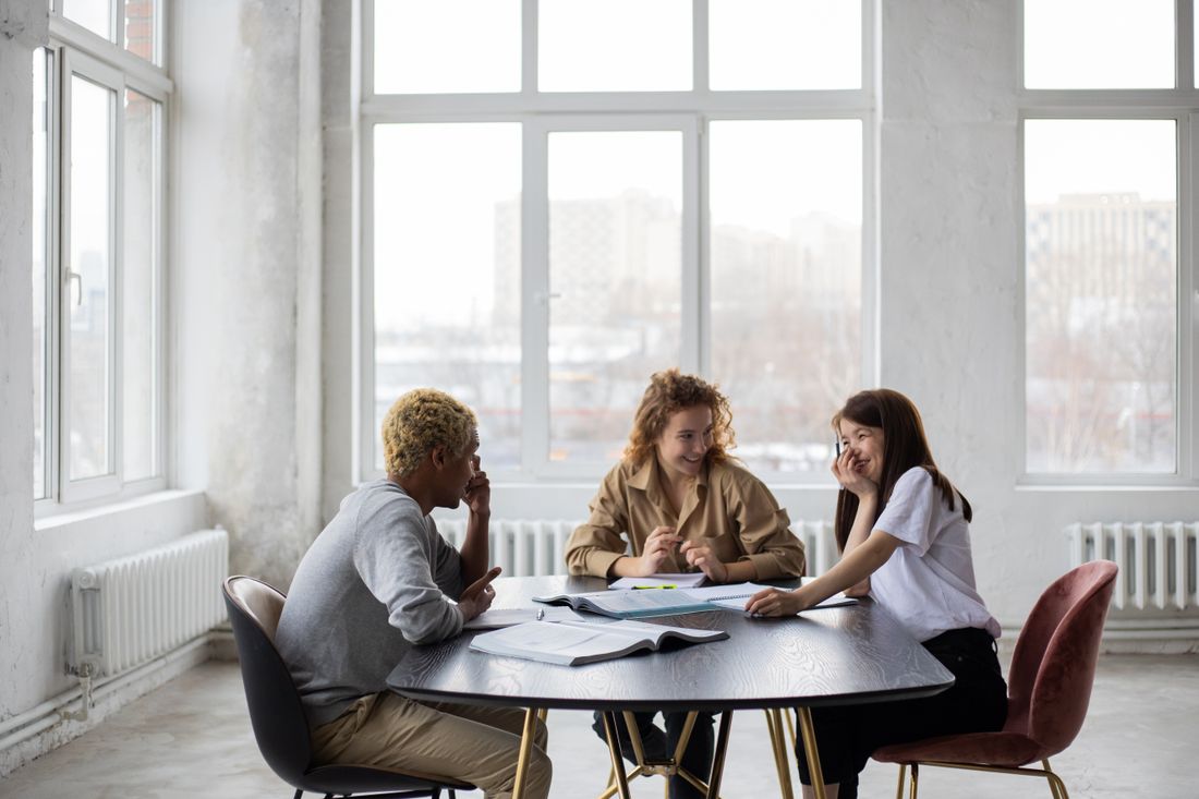 Three students talking and studying together in a bright classroom.